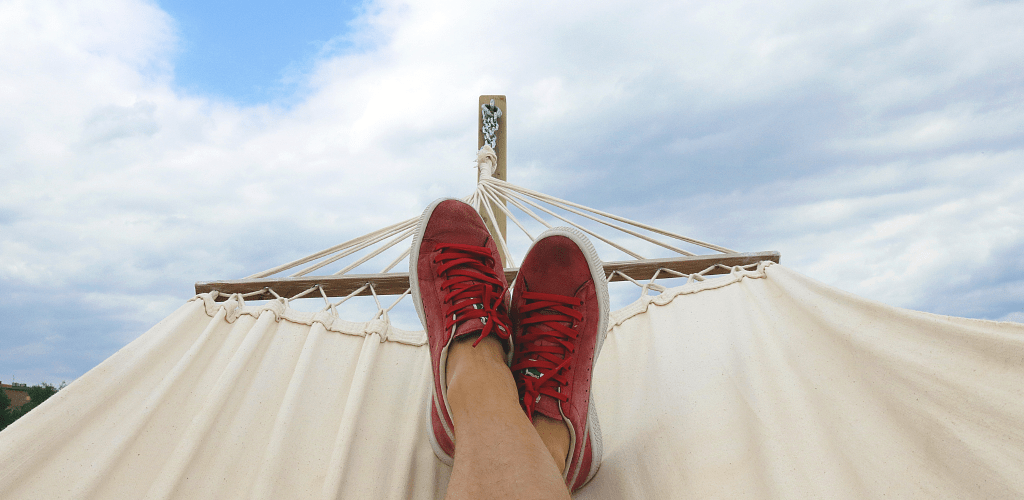 Eine Person mit roten Schuhen entspannt sich unter blauem Himmel in einer Hängematte.
